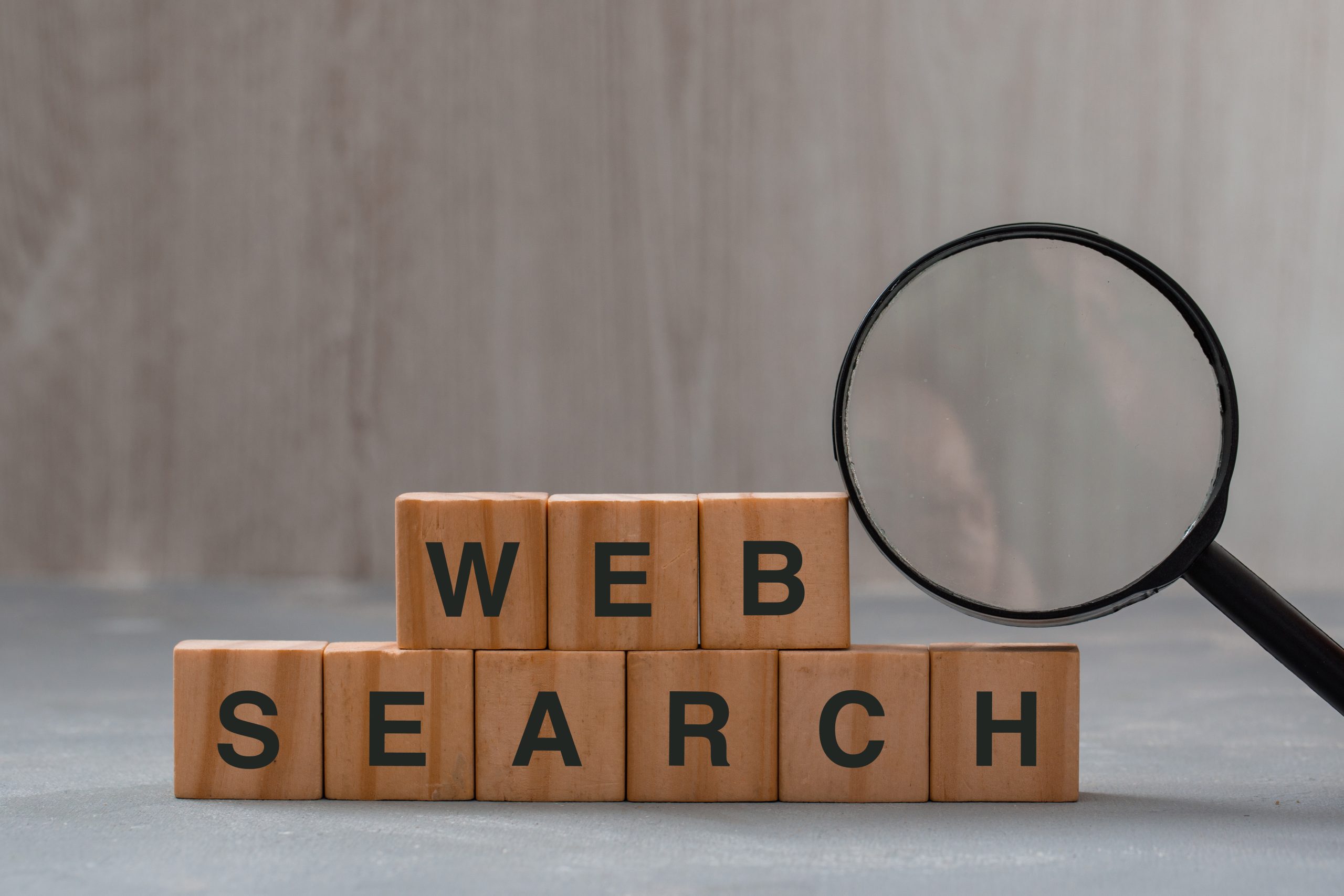 Keyword research strategy concept with magnifying glass, word web search on wooden cubes on plaster and wooden background.