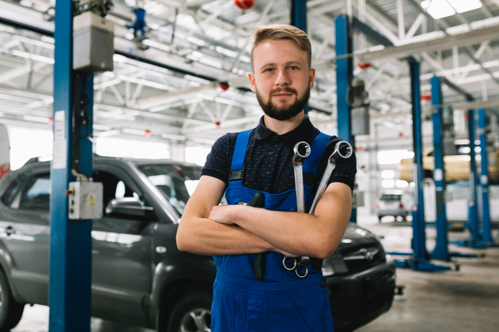 An auto repair mechanic, holding his tools, post a photo inside his physical shop.