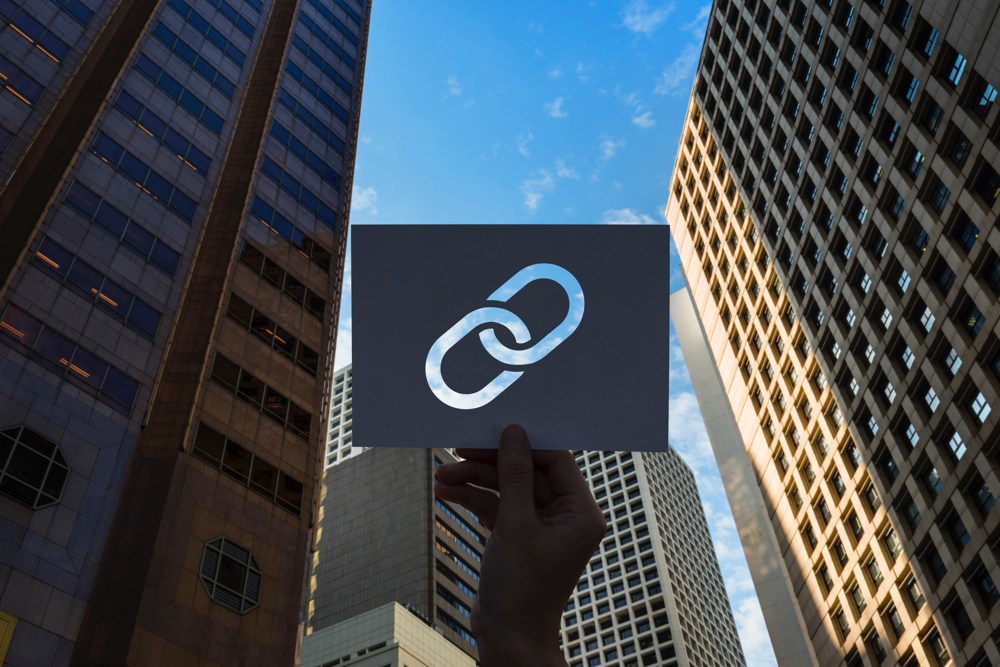 A link icon perforated in paper, facing upwards between buildings, in representation for internal linking for enterprise SEO strategy.