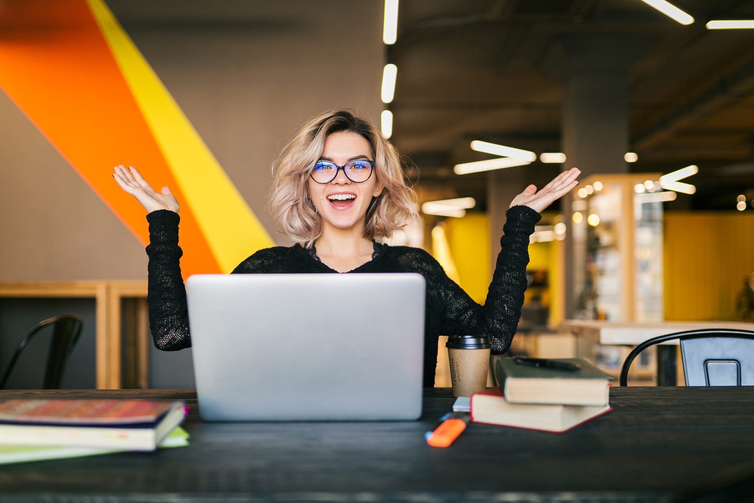 An excited young woman, sitting in an office room, probably got a freelance job.