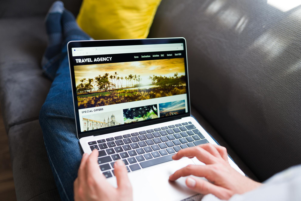 A traveller booking in a travel agency website, using his laptop, while laying on a couch.
