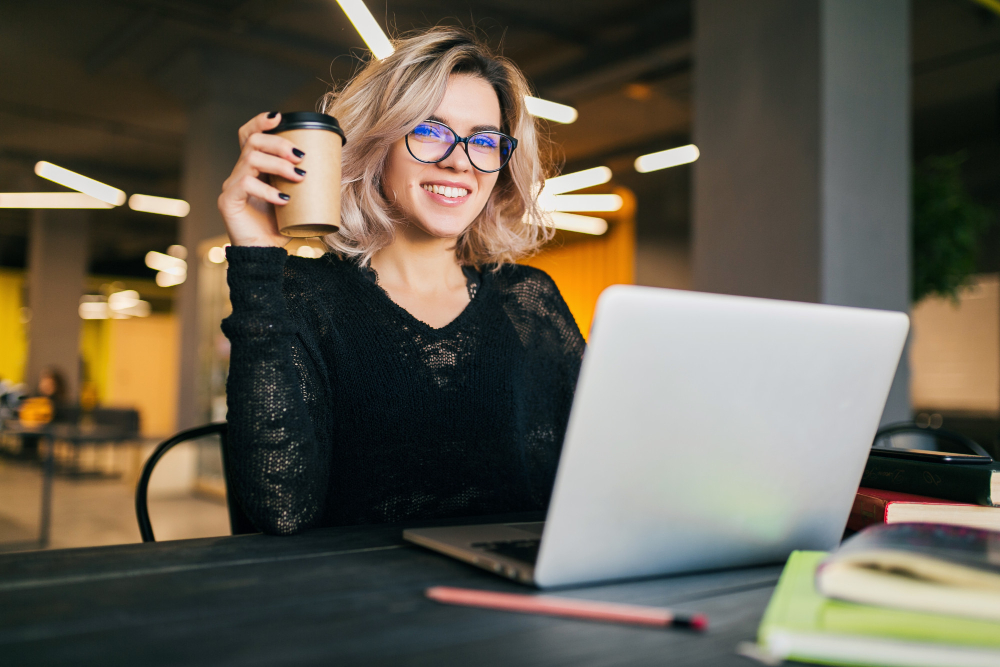 Portrait of an SEO writer sitting on a table, with her laptop on, holding a cup of coffee.