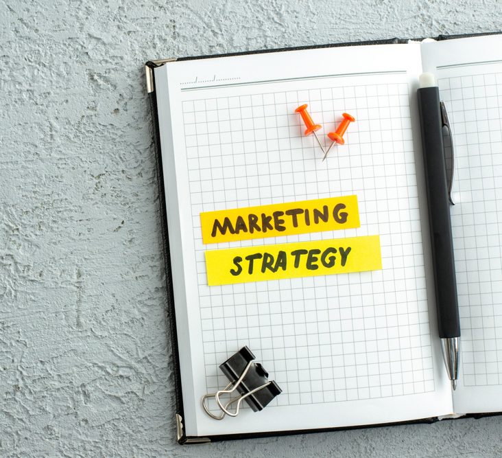 Top view of a digital marketing strategy and concept, written in an open white notebook with a pen in the middle