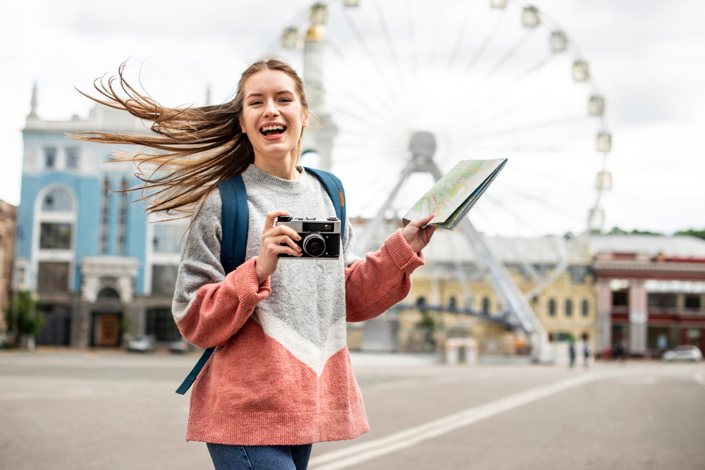 A beautiful young traveller in Sydney, with a camera and map in hand, pose for a shot in front of a Ferris wheel.