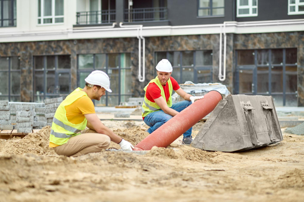 Two pool builders inserting a huge pipe in a pool construction site.