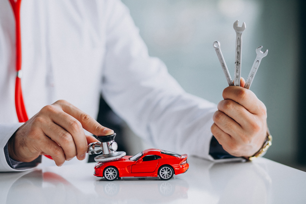 A business owner in casual suit, holding some tools, with a car miniature on the table.