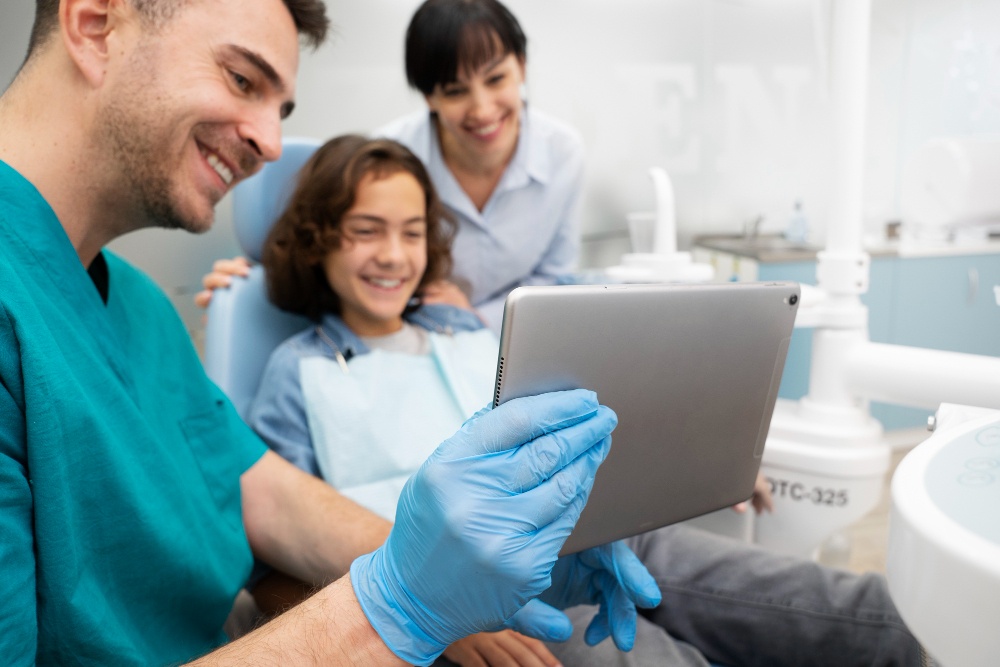 A close up shot with a dentist, discussing some dental stuff using an iPad to a young boy patient, assisted by his mom.