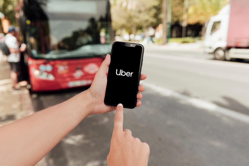 An index finger pointing to an Uber app, while holding her smartphone using her left hand.