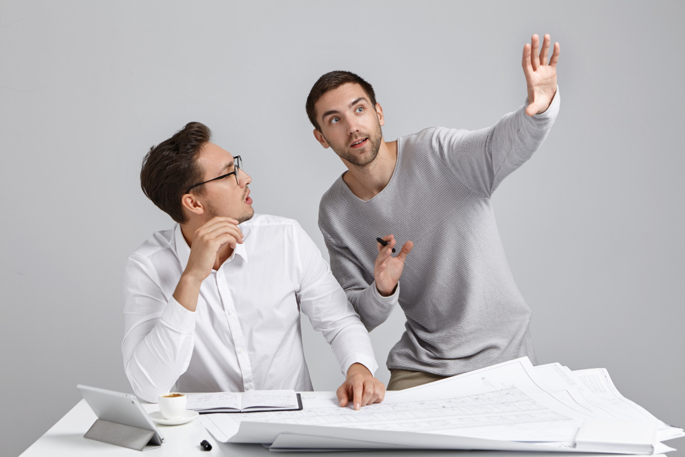 Two engineers in casual suits, visualizing on PPC advertising for construction businesses strategy, with drawing plans laid out on top of the table.