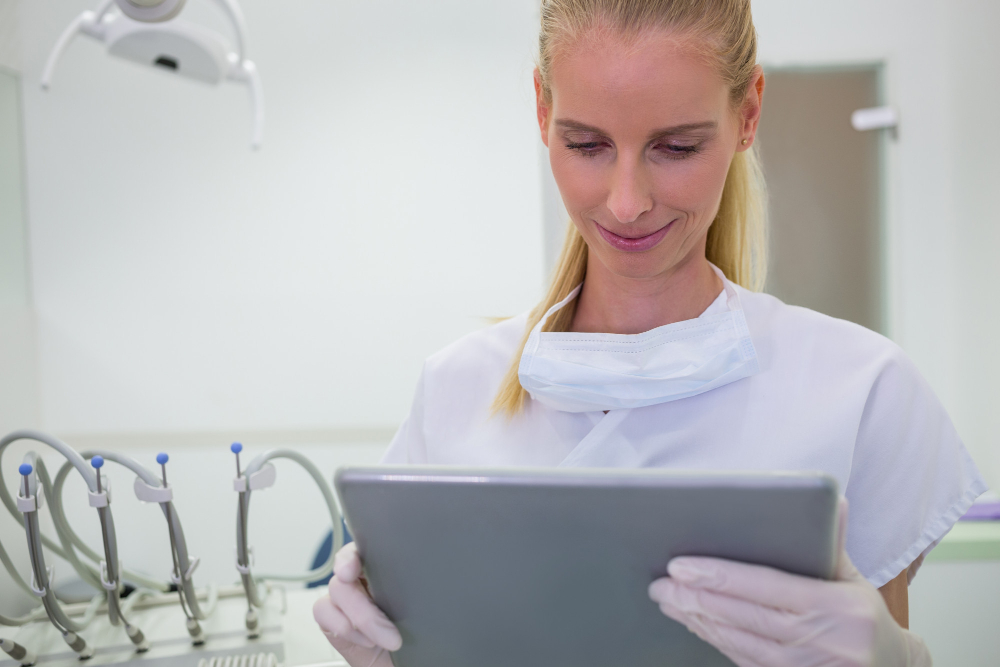 A young female dentist, in full white suit and gloves, working on some content marketing for dentists campaign strategy, using her iPad.