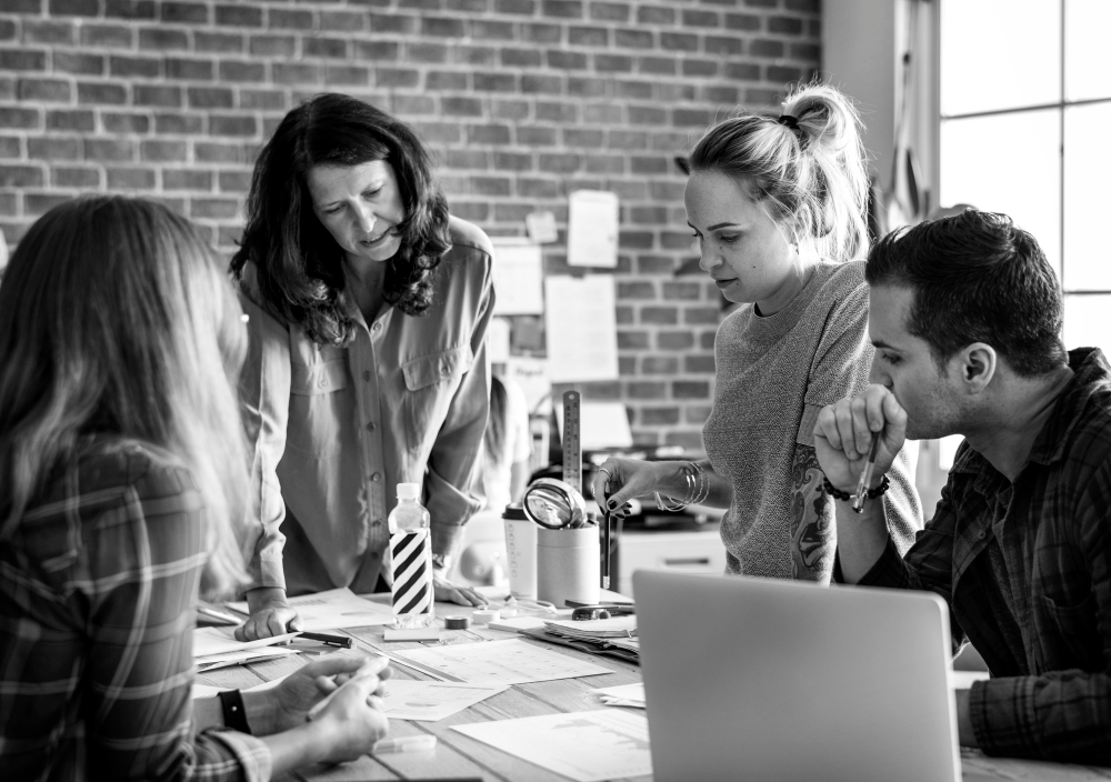 Group of marketers in black and white photo, gathered around for a brainstorming session.