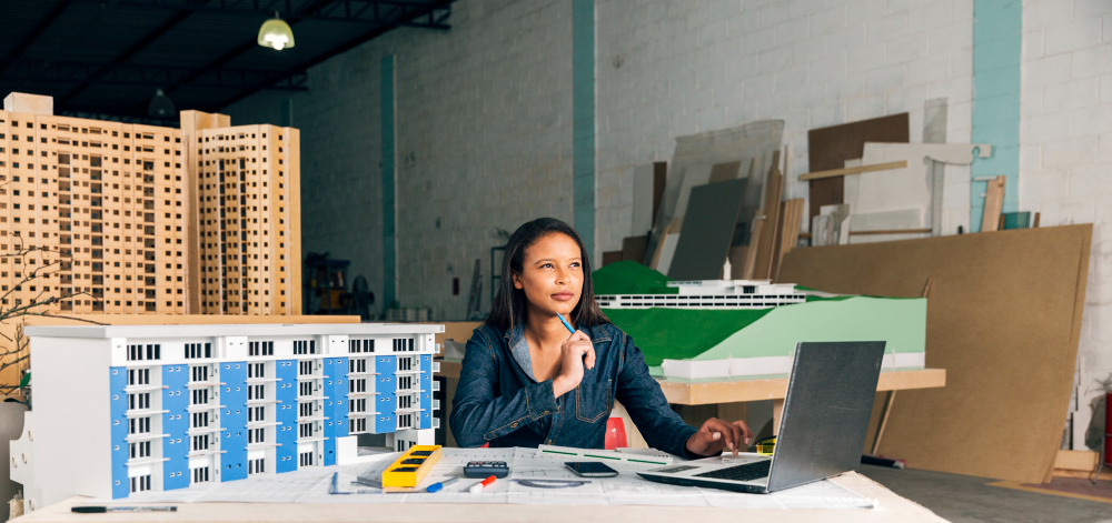 An exterior designer, in casual clothing, sitting in her office, thinking about Local SEO for exterior designers strategy campaign, while pointing a pencil on her chin.