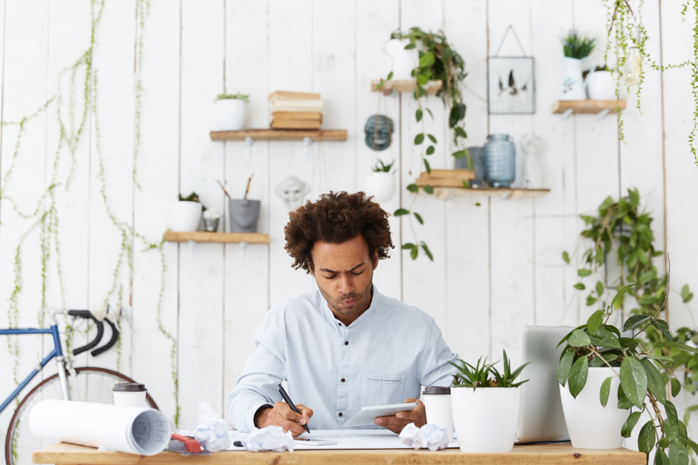 A designer, sitting on his desk, while analyzing the impact of user experience on SEO for interior designers strategy, using his digital tablet.