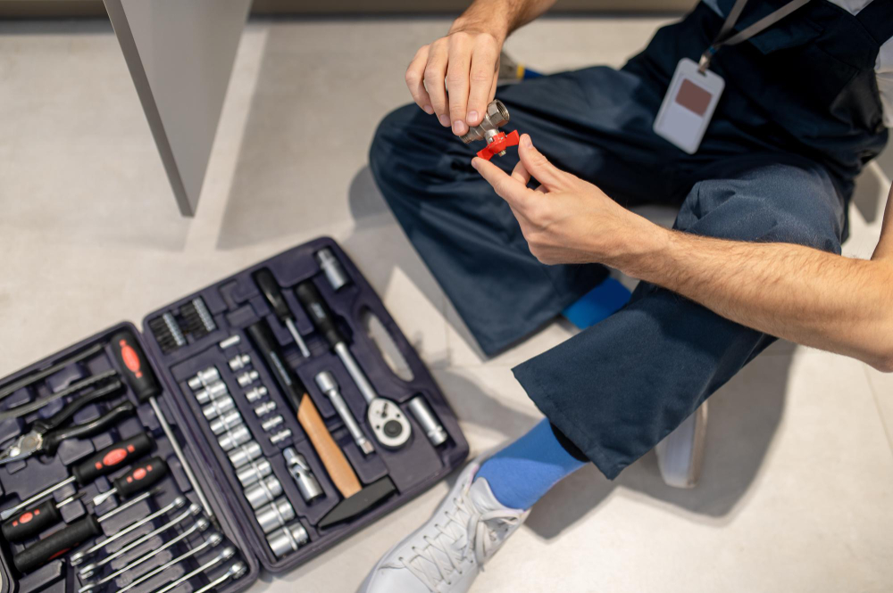 Top view of a plumber in jumpsuit, fixing a faucet pipe, with tool box in front of him.