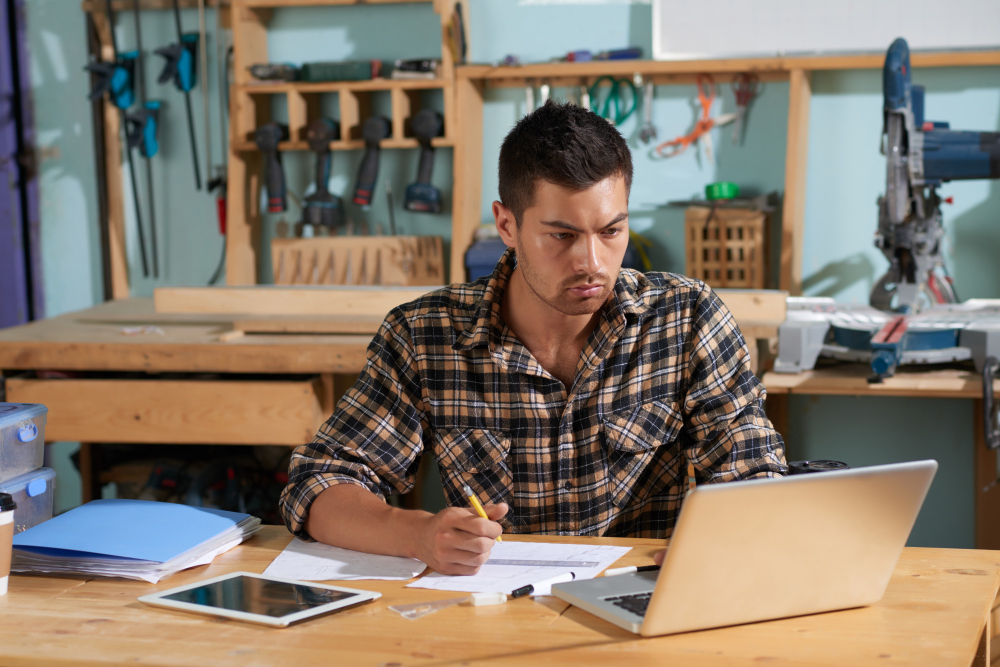 A plumber on his working table, jotting some notes from his laptop on content marketing strategy for his plumbing services business in Sydney, with tools on the background.